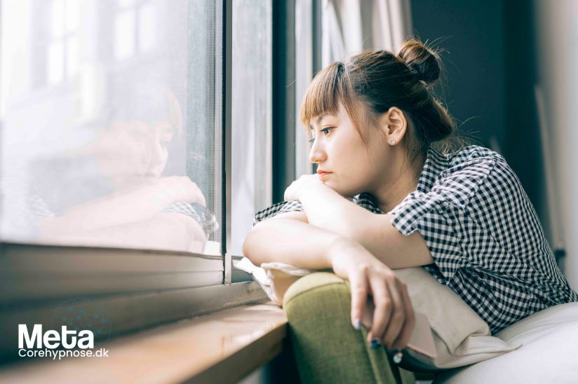 Asiatisk kvinde sidder og kigger ud af vinduet. Depression behandling hos corehypnose.dk